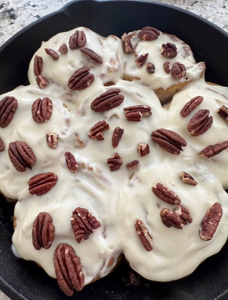 Baked goods with white icing and pecans in a black pan