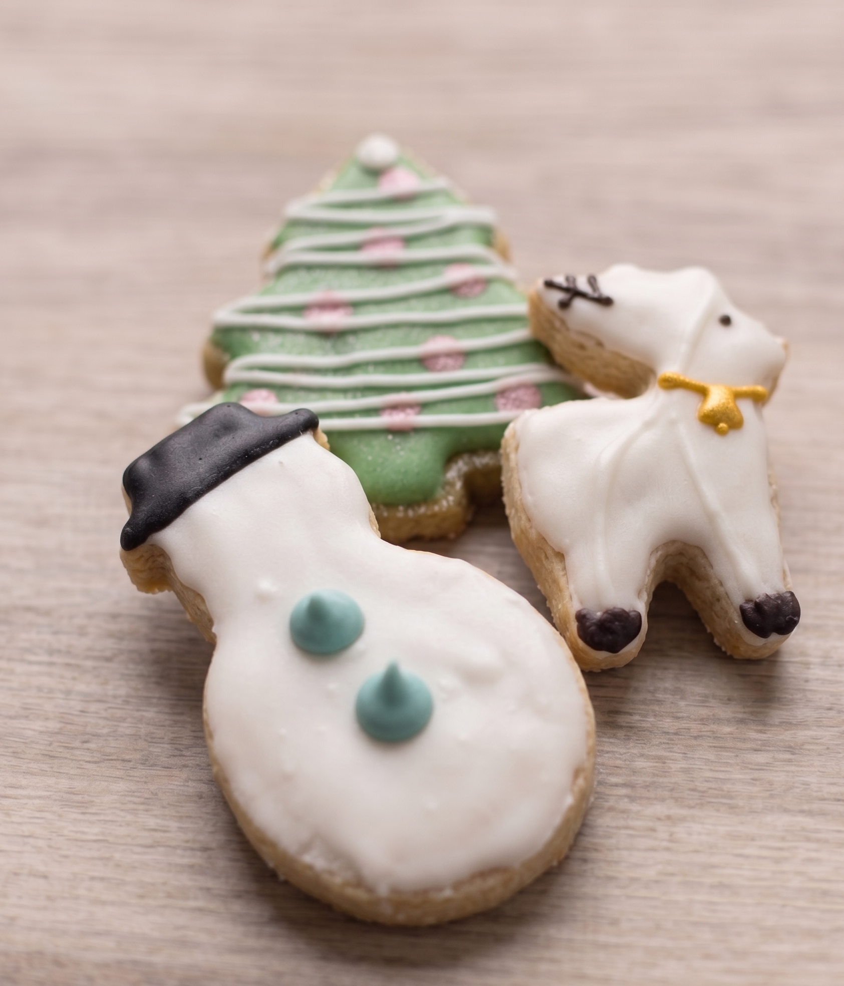 Decorative cookies shaped like a snowman, Christmas tree, and dog on a wooden surface.