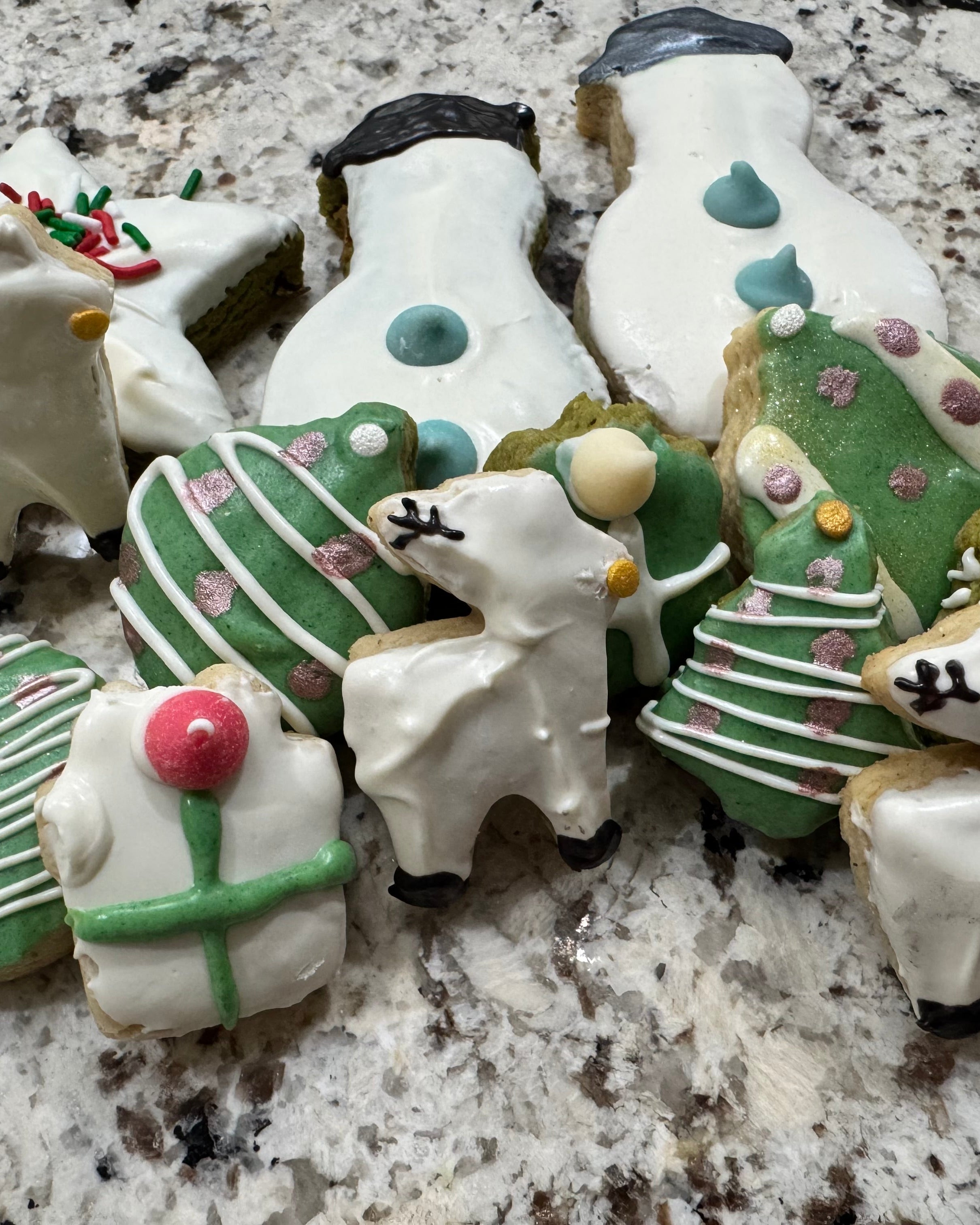 Decorative cookies shaped like Christmas trees, presents, and other festive items on a marble surface.