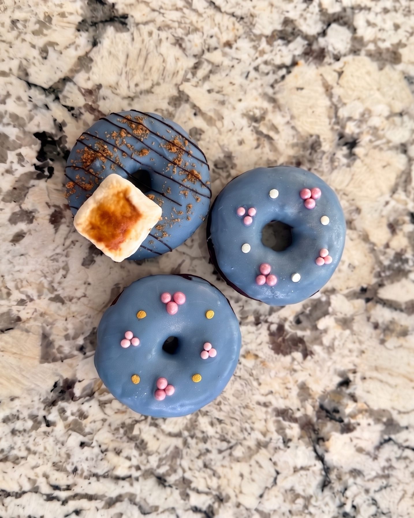 Three blue donuts with pink sprinkles on a granite countertop